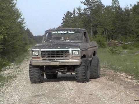 1995 Ford Bronco - This lifted Ford pickup truck is driving on a gravel road surrounded by trees.