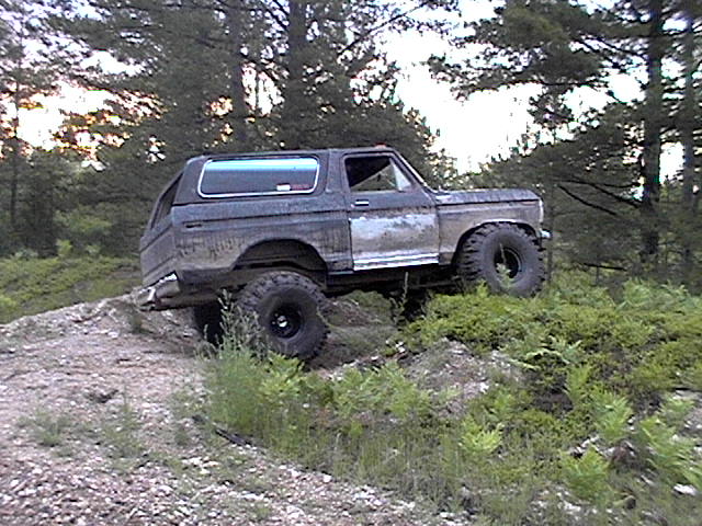 Dark gray Ford Bronco with a white cap driving off-road on a dirt hill