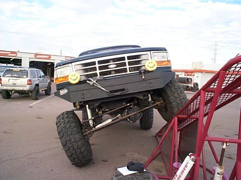1994 Ford Bronco - Modified Ford Bronco with large tires is positioned on a red ramp, with another SUV visible.