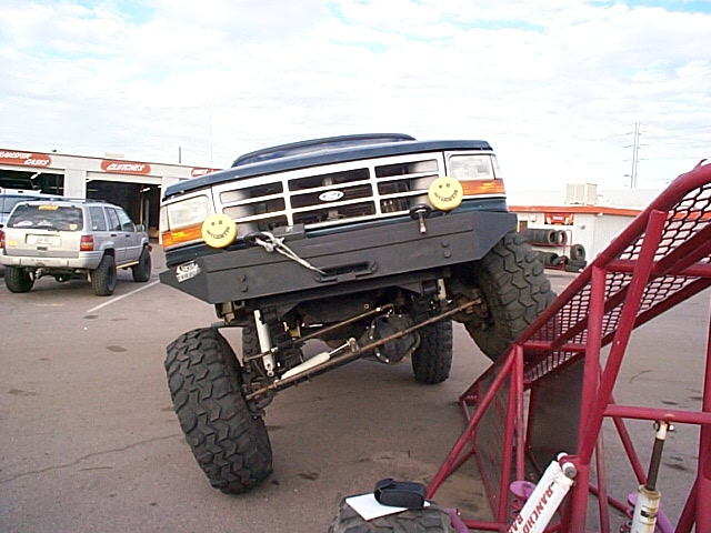 Lifted dark Ford SUV, front view, big mud tires and solid axle in a lot