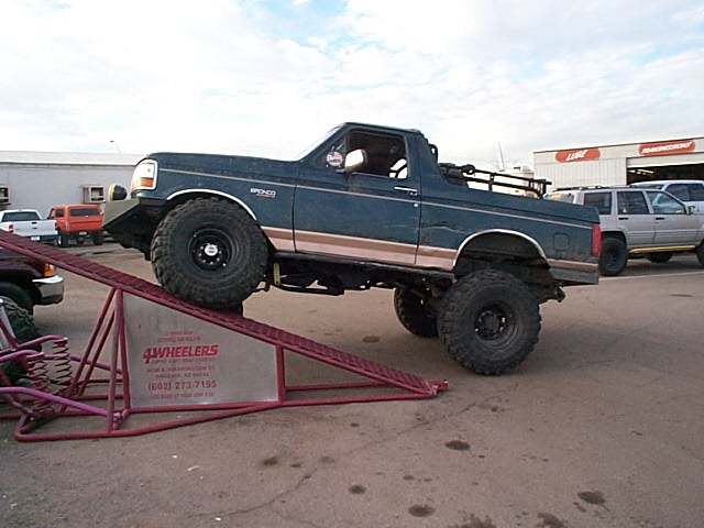 Lifted green Ford Bronco with top off climbing a red RTI flex ramp
