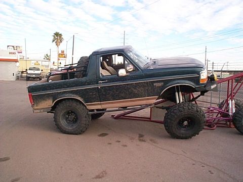 1994 Ford Bronco - Modified dark green Ford Bronco with off-road tires and suspension, parked outdoors.