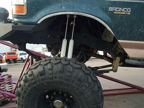 1994 Ford Bronco - Close-up of a modified 1994 Ford Bronco's suspension and tire, with other vehicles in the background.