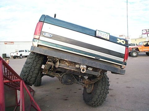 1994 Ford Bronco - Modified Ford truck with oversized tires is angled on a red ramp, with other vehicles in the background.