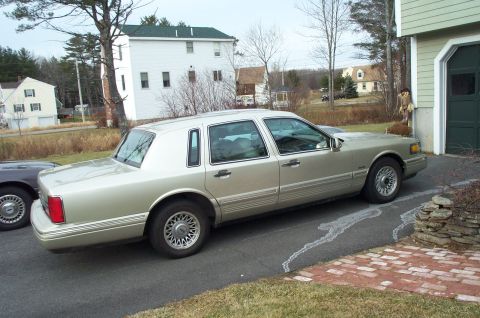 2001 Ford Crown Victoria - A beige Lincoln Town Car is parked in a driveway next to a garage on a cloudy day.