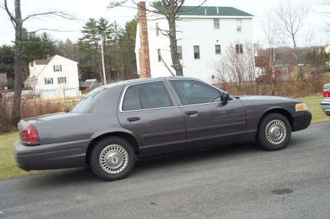 2001 Ford Crown Victoria - A gray 2001 Ford Crown Victoria sedan is parked on an asphalt surface with houses in the background.
