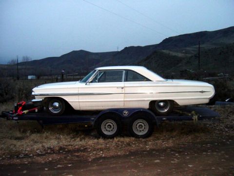 1964 Ford Galaxie - A white coupe is loaded onto a trailer, ready for transport. The vehicle has a distinctive side trim.