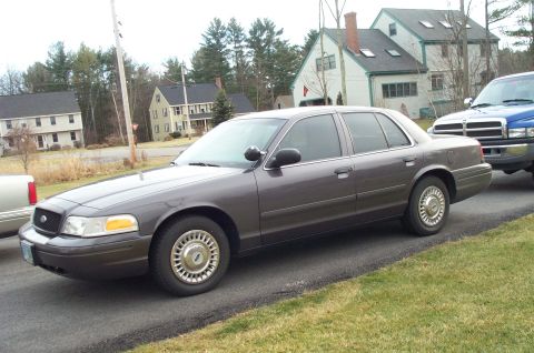 2001 Ford Crown Victoria - A gray 2001 Ford Crown Victoria sedan is parked on the side of the road next to a blue pickup truck.