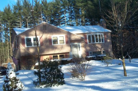2001 Ford Crown Victoria - A residential house is covered in snow, with pine trees in the background and bare trees in the foreground.