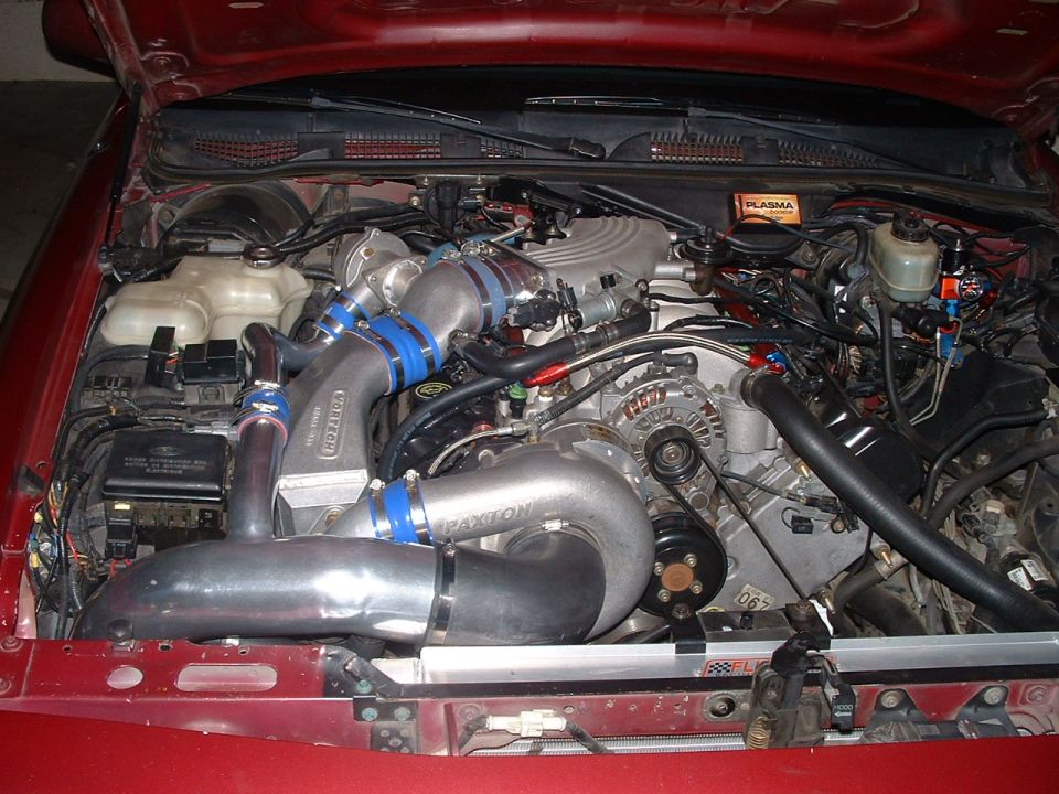 Red engine bay with twin turbochargers, intercooler piping, and custom intake. Paxton supercharger visible