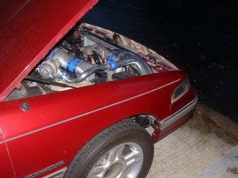 1992 Ford Crown Victoria - The engine bay of a red 1992 Ford Crown Victoria features a twin-turbo setup with prominent intercooler piping.
