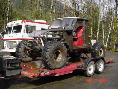 1985 Ford Bronco - A heavily modified off-road vehicle with large tires is loaded onto a trailer, with an RV parked behind it.