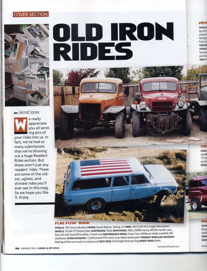 light blue station wagon with American flag on roof, parked on dirt with two old trucks behind it