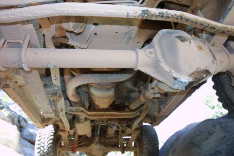 1987 Ford Bronco - The underside of a vehicle reveals its drivetrain components, including a substantial differential and exhaust system.