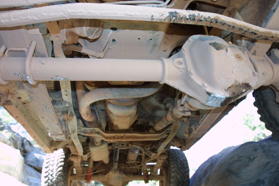 Underside of a 4x4 truck showing front axle, driveshaft and differential coated in tan dust.