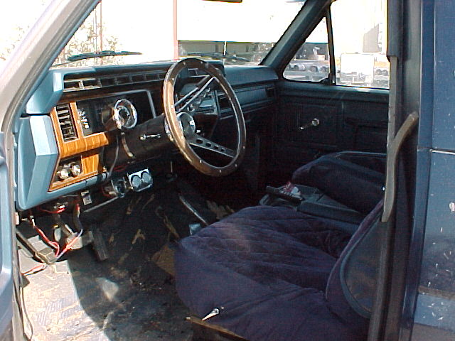 Interior view of a blue truck with wood-grain trim and aftermarket steering wheel