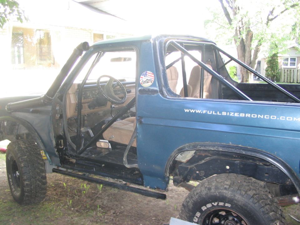 Teal Ford Bronco with doors and top off, black roll cage, snorkel and rock sliders