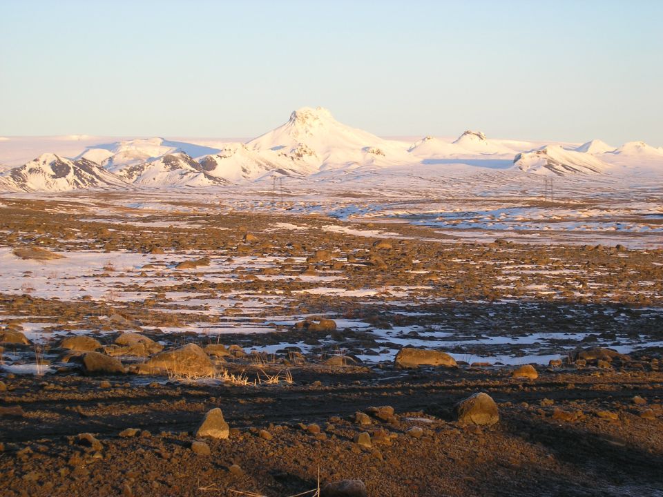 Snow-covered mountain rising over a barren rocky tundra plain at sunrise