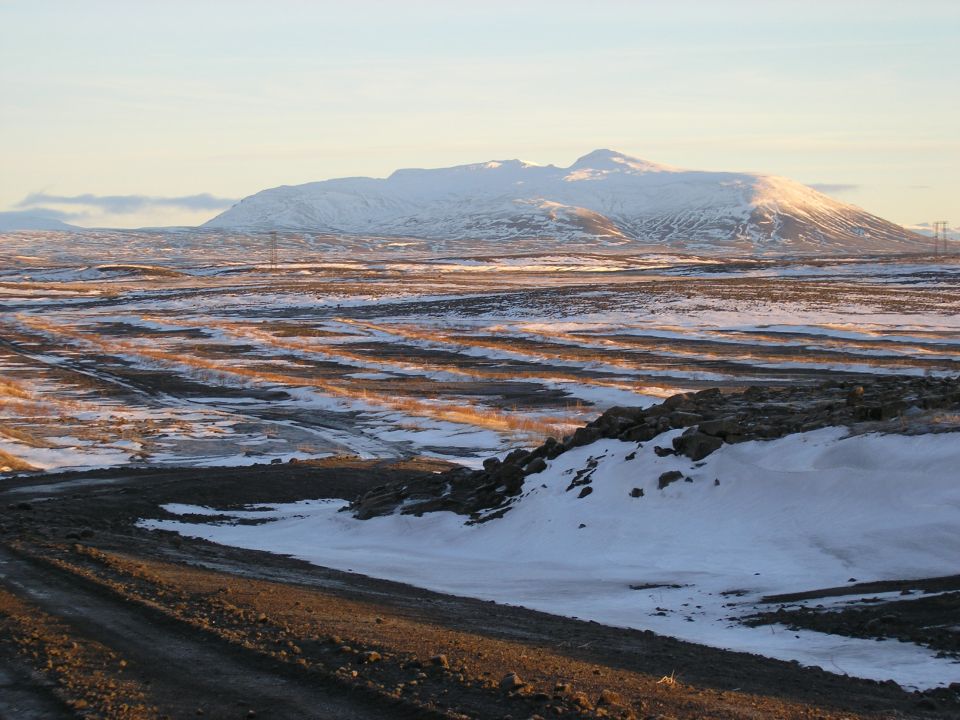 Snowy ridge with a dirt track cutting across a frozen landscape in low sun