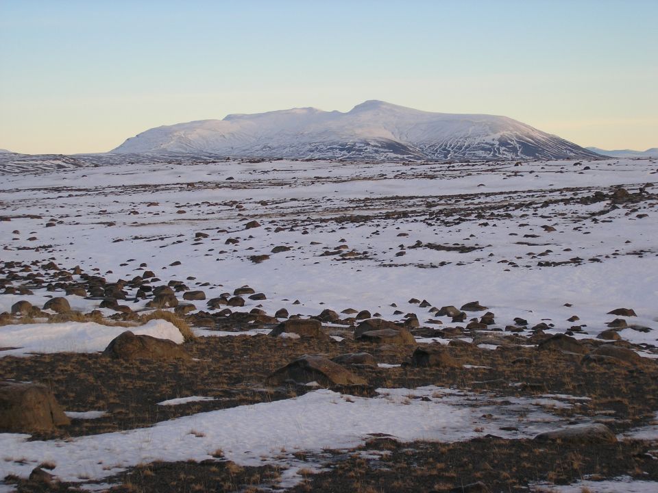 Flat-topped snowy mountain over a rocky snow-covered plain at dusk