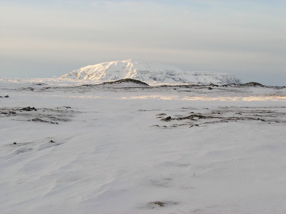 Sunlit snow-covered plateau mountain over a windblown frozen plain