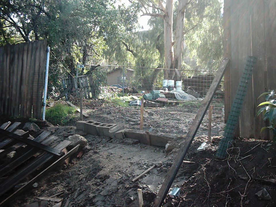 Construction site with cinder blocks, wood, and fencing under trees