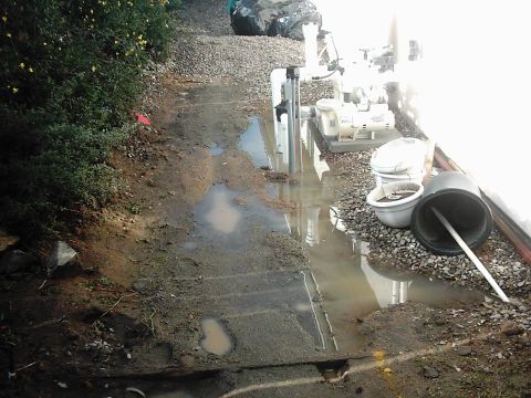 1978 Ford Bronco - A water pump and associated plumbing are visible next to a building, with puddles on the ground.