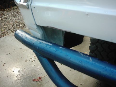 1978 Ford Bronco - Detail shot of a vehicle's rear end, showing a blue tubular bumper and white body panel.