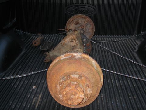 1989 Ford F-150 - A heavily rusted rear axle assembly is chained down in the bed of a truck.