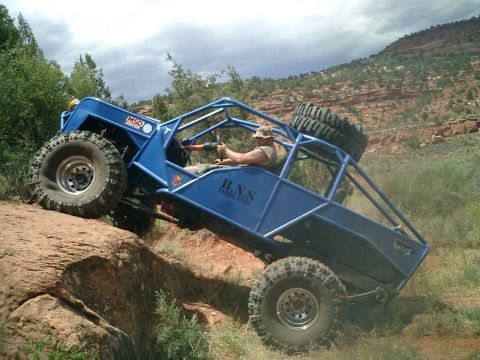 1979 Ford Bronco - A custom-built buggy navigates a rocky off-road trail under a cloudy sky.