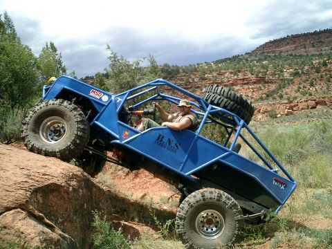 1979 Ford Bronco - A heavily modified off-road buggy navigates a steep, rocky terrain under a cloudy sky.