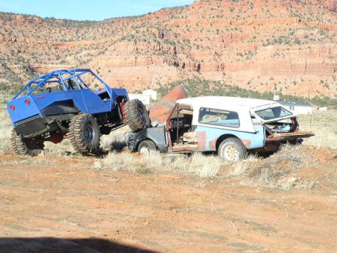 1979 Ford Bronco - A custom-built off-road buggy is perched precariously atop a derelict SUV in a dry, rocky terrain.