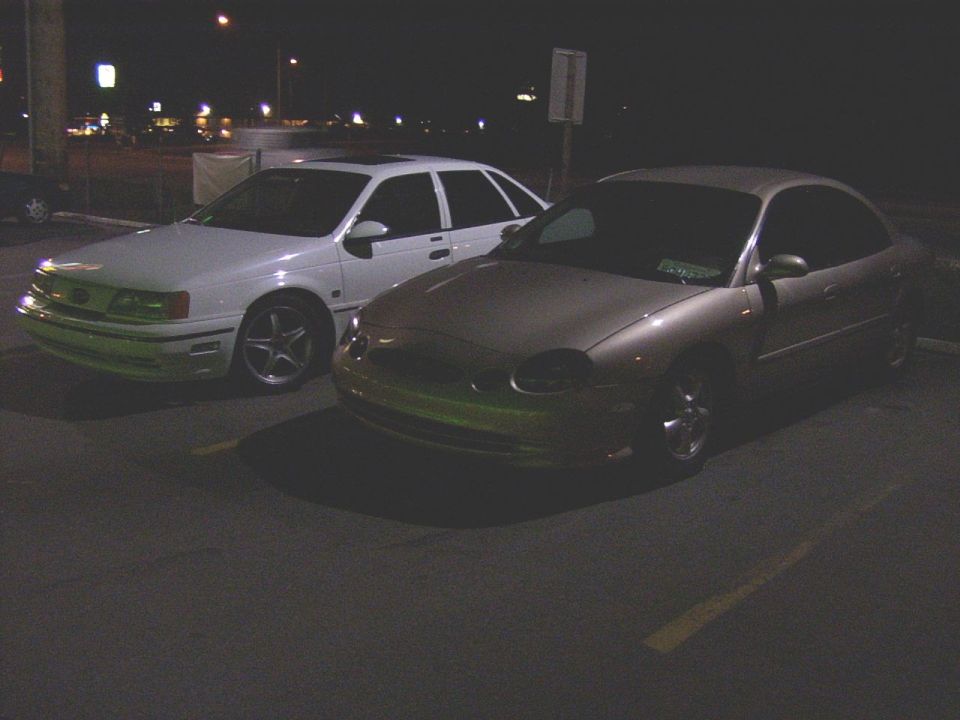 Gold sedan parked next to a white sedan at night