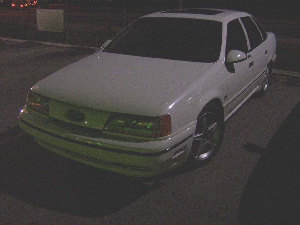 White sedan parked at night, front quarter view. It has aftermarket wheels and a sunroof