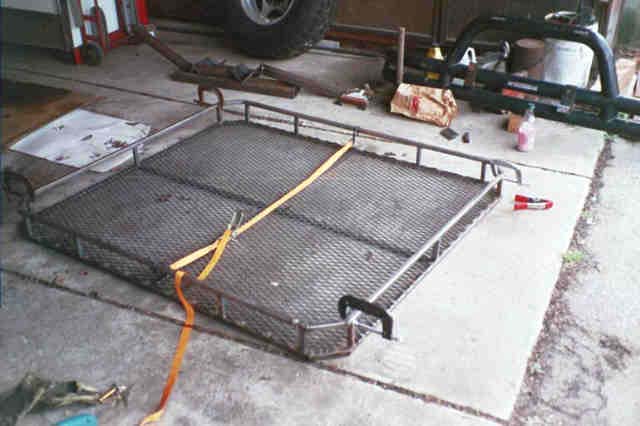 Steel mesh-floor roof rack basket lying on a garage apron with a ratchet strap