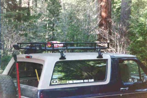 1994 Ford Bronco - Rear view of a 1994 Ford Bronco parked in a wooded area, equipped with a roof rack.