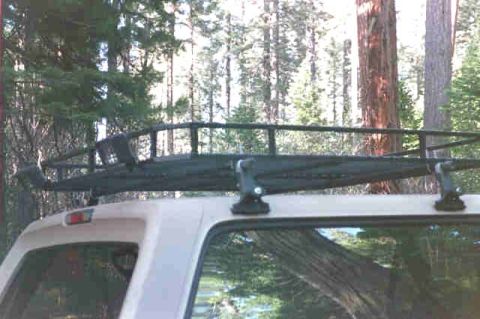 1994 Ford Bronco - A roof rack system is mounted on the top of an SUV, surrounded by tall trees.
