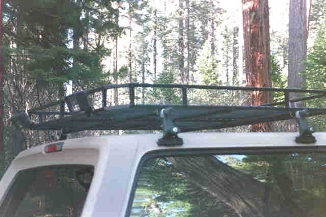 Black tubular basket roof rack on white SUV hardtop in a pine forest
