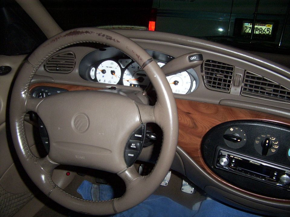 1998 Mercury Sable interior with tan dashboard, wood trim, and a worn steering wheel. The instrument cluster and radio are visible