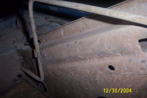 1979 Ford F-150 - Close-up view of a heavily rusted vehicle frame section with visible bolts and pipes.