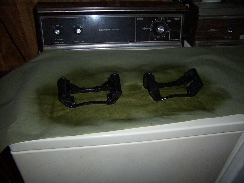 Two black brake caliper brackets on a green paper towel, with a Kenmore dryer in the background