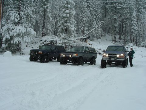 1989 Ford Bronco - Three SUVs are parked in a snowy forest clearing, with one vehicle appearing to be a Ford Bronco.