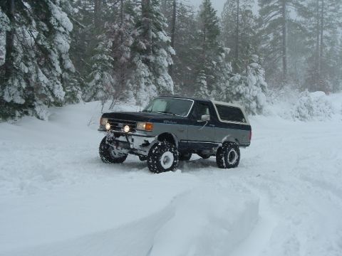 1989 Ford Bronco - A 1989 Ford Bronco navigates a snowy forest road with its suspension lifted and equipped with off-road tires.
