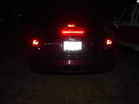 2000 Ford Taurus - The rear of a Ford sedan is illuminated by its brake lights, with another vehicle partially visible to the side.