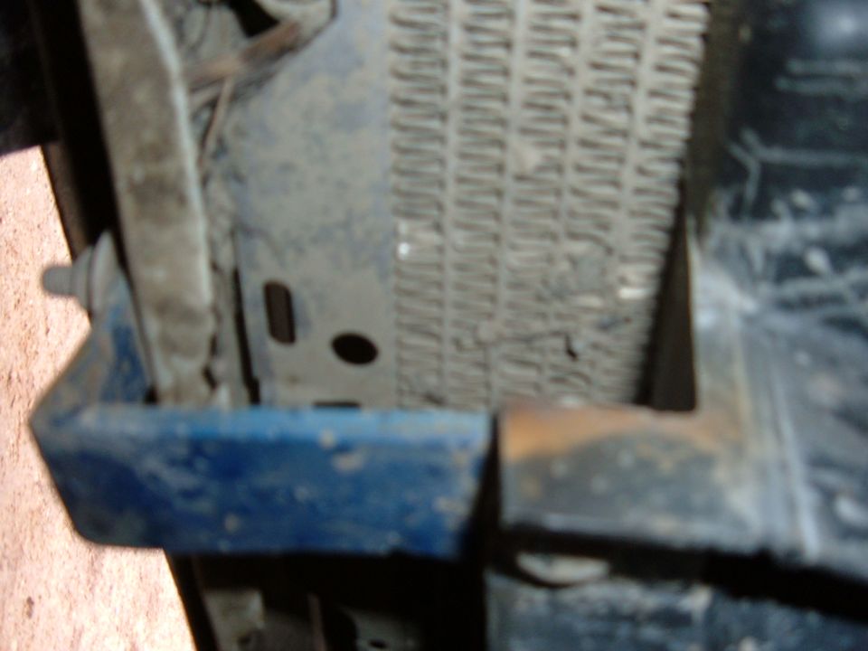 Close-up of a vehicle's radiator and a blue painted metal bracket