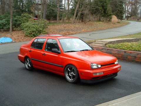 1994 Volkswagen Jetta - Red sedan with aftermarket wheels parked on a paved driveway in front of a house.