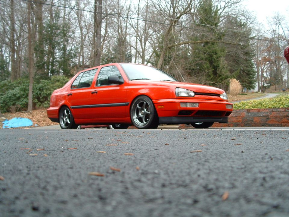 Low front three-quarter shot of red slammed VW Jetta III sedan on dark wheels