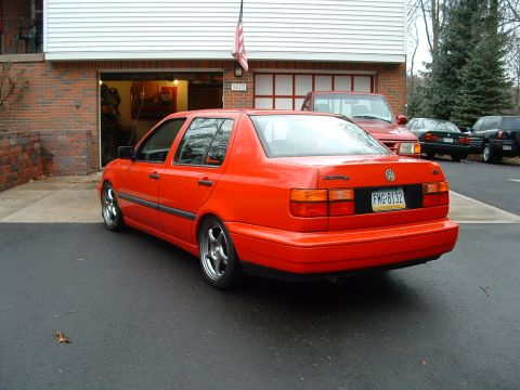 1994 Volkswagen Jetta - Orange sedan with aftermarket wheels parked in driveway next to a red truck.