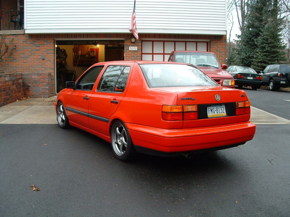 Slammed red VW Jetta III sedan on polished-lip wheels, rear three-quarter in a driveway