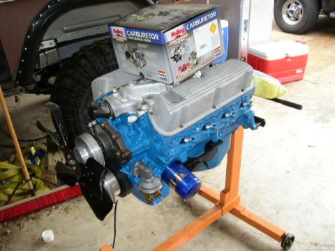 1995 Ford Bronco - A blue engine with silver valve covers sits on an orange engine stand, with a carburetor box on top.